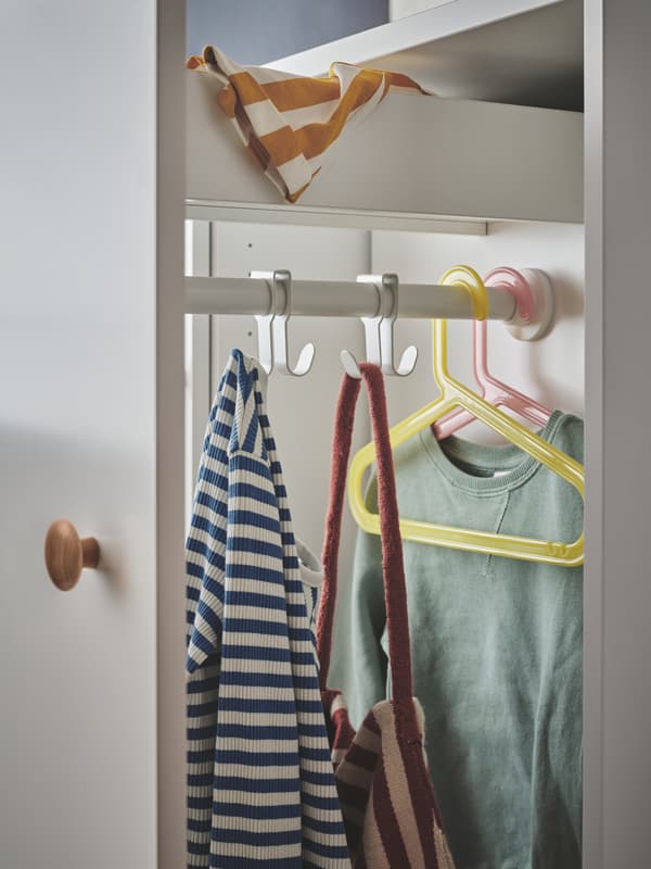 The white SMÅSTAD pull-out storage unit with a top drawer and hooks and hangers holding children’s clothes and a bag.