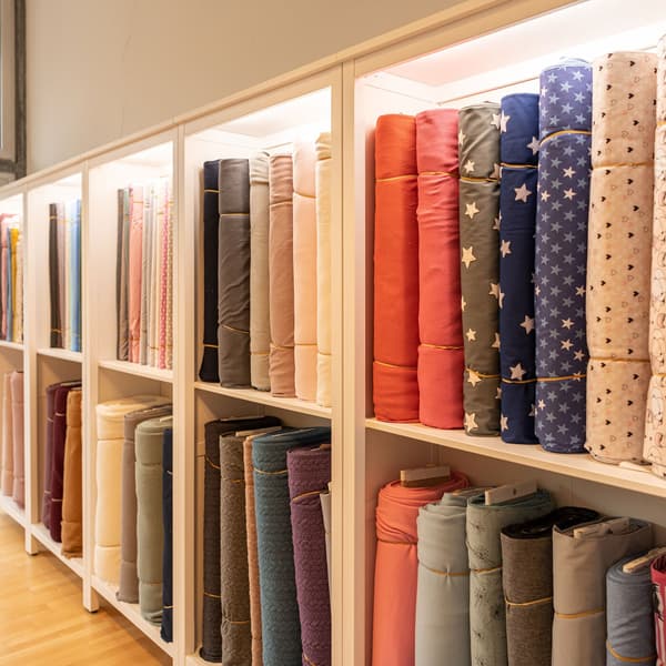 There are many different bales of fabric on end on a shelf.