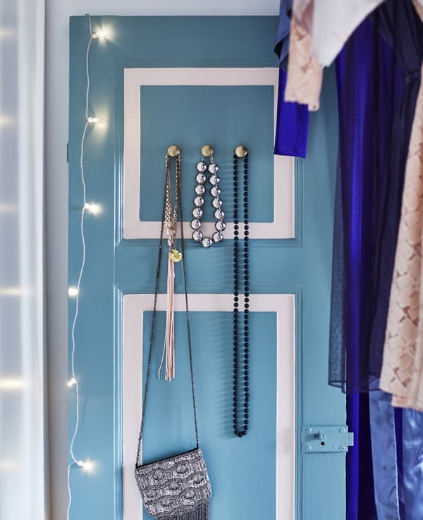 There is an antique wooden door, painted light blue and white, to which handles have been added for hanging scarves and a bag.
