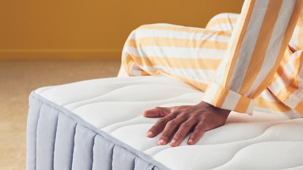 There's a man sitting on a mattress and putting his hand on it.