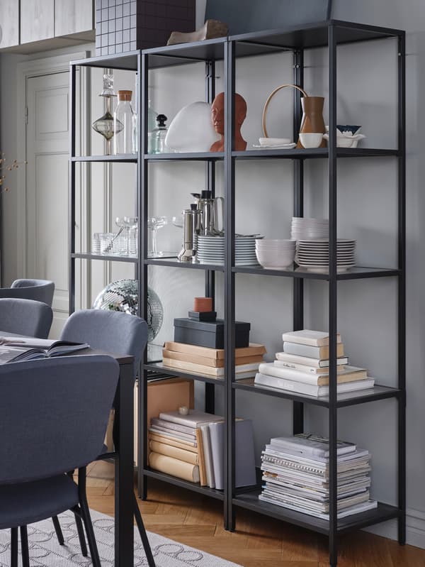 Three black shelving units stand together to create a larger unit where dinnerware and decorative items are stored.