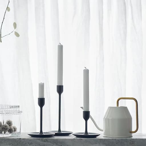 Three candlesticks in different heights are shown against a white background, with a watering can and some glass containers.