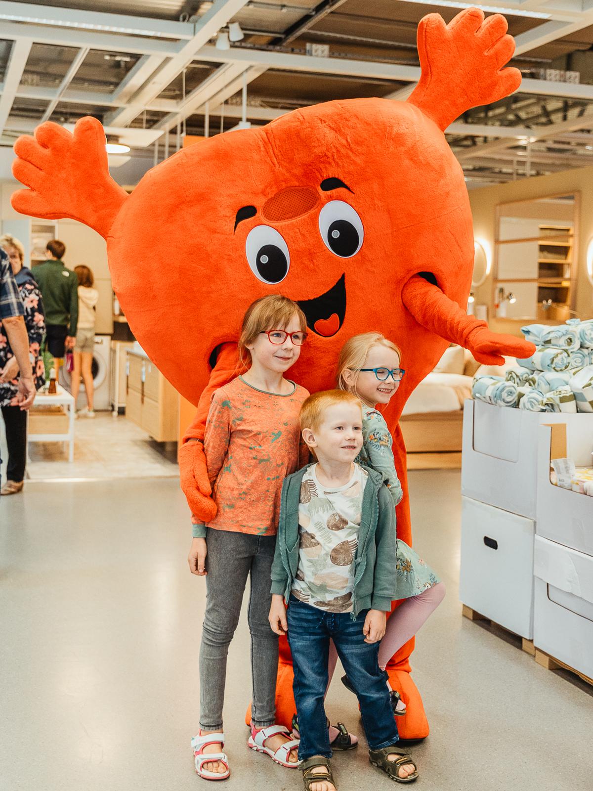 Three children pose with a large red heart mascot in an IKEA store.