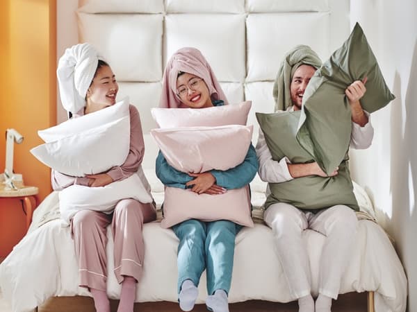 three friends in pajamas seated on end of bed hugging pillows