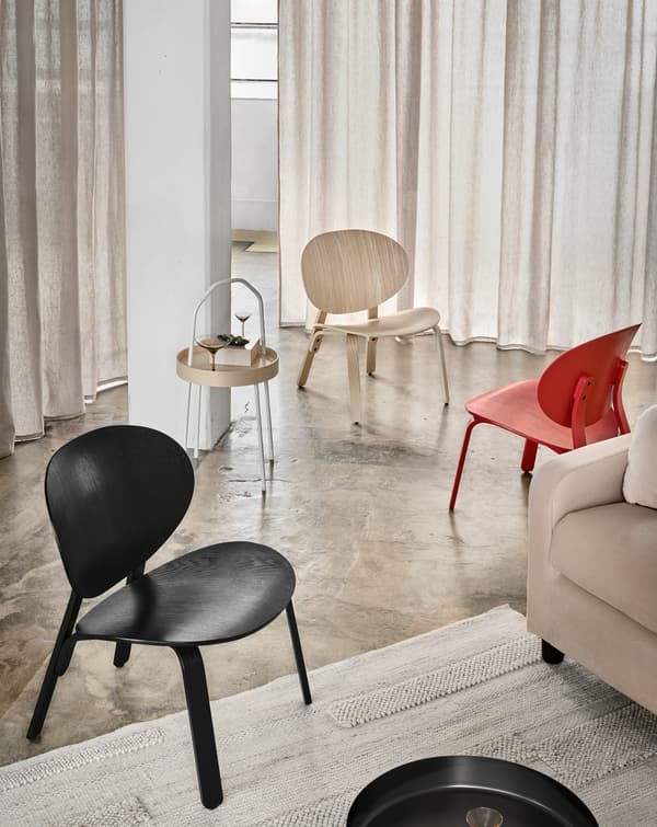Three FRÖSET chairs in white, red and black stained oak veneer standing in a haphazard way near a sofa.