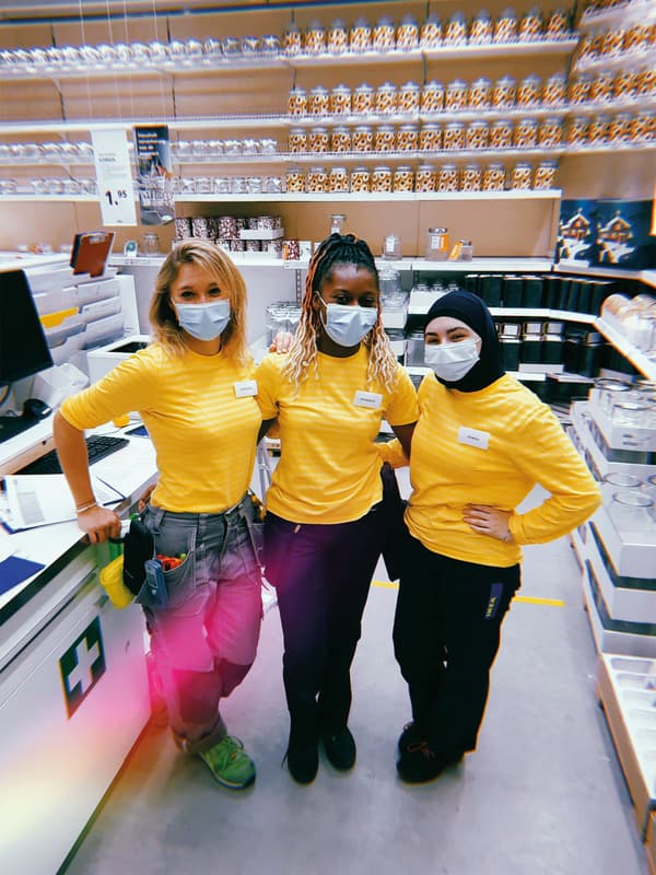 Three IKEA co-workers stand side by side, wearing yellow shirts and face masks.