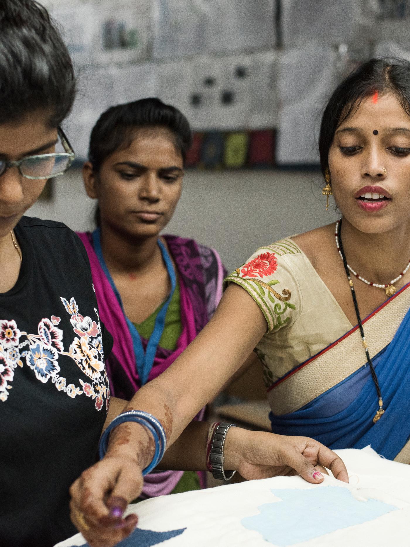 Three Indian weavers in traditional dress discussing the design of a rug.