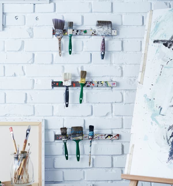 Three magnetic knife racks holding paintbrushes on the wall of an art studio.