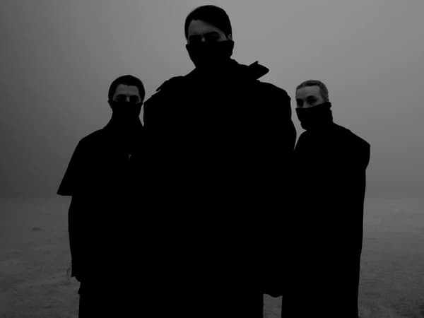Three men wearing black clothing with masks covering the bottom of their face, against a gray background.