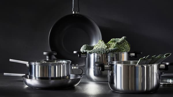 Three MIDDAGSMAT pots with lids in stainless steel with a pan on a black background.