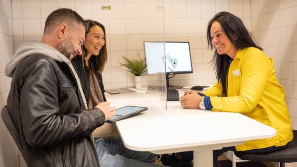 Three people are sitting at a table in an office setting, with a computer screen in the background.