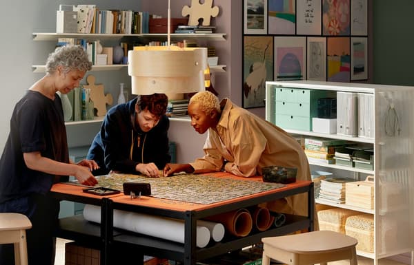 Three people by table looking at fabric under wooden lamp in well-organised home full of colours