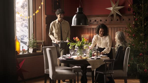 Three people gather round a round INGATORP table decorated with fresh flowers to eat a holiday meal together.