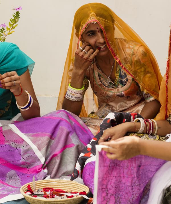 Three people sitting and working on colourful fabrics together.