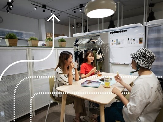 Three people sitting around a table in a showroom‑like space, talking and looking at a magazine.