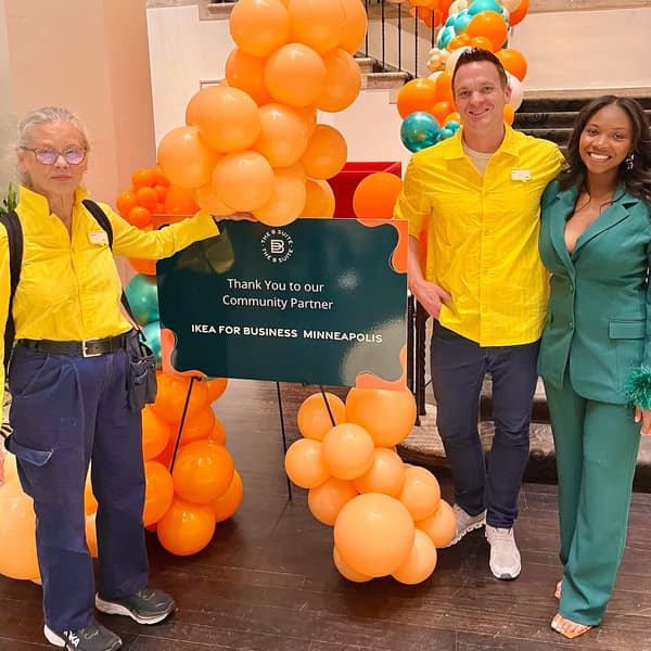 Three people, two IKEA co-workers and a woman in a green suit standing with a sign and smiling.
