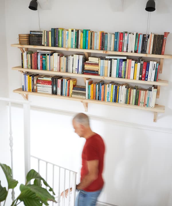 Three shelves of books on a white wall above a staircase.