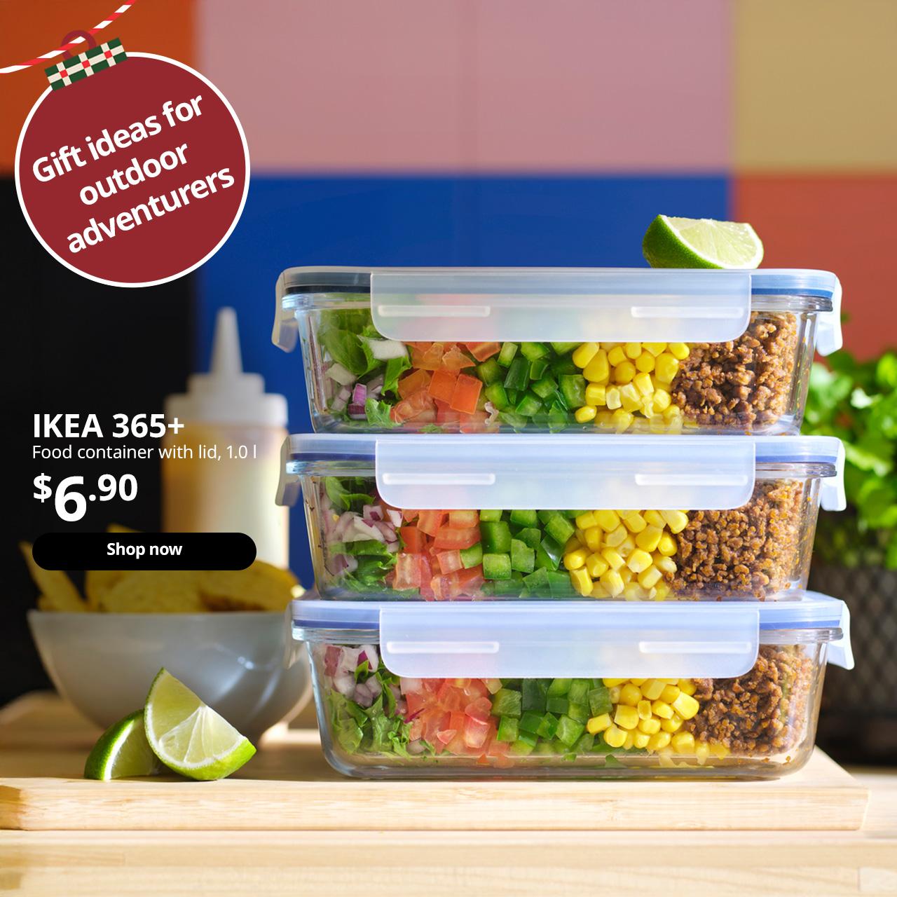 Three stacked IKEA 365+ food containers with layered salad ingredients are placed on a countertop with a colourful wall.