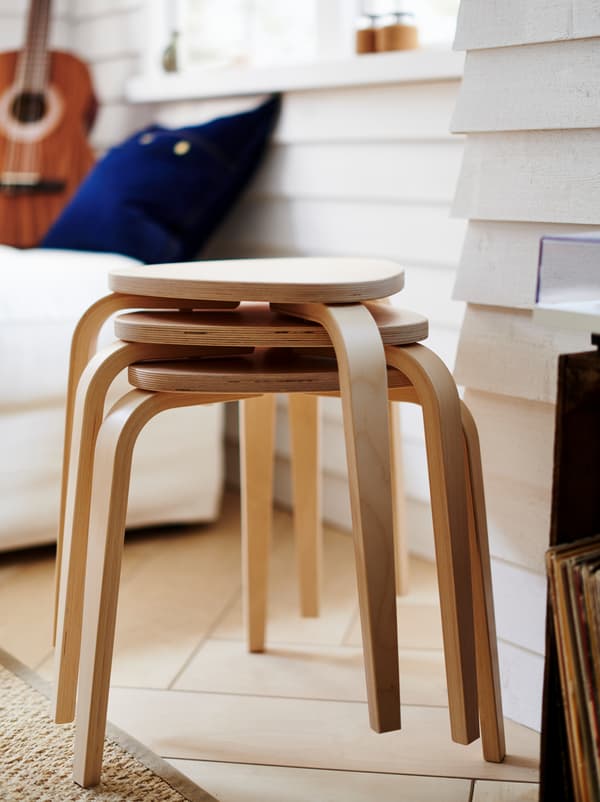 Three stacked KYRRE stools placed by a white clapboard wall, a few feet from a white sofa with a guitar on it.