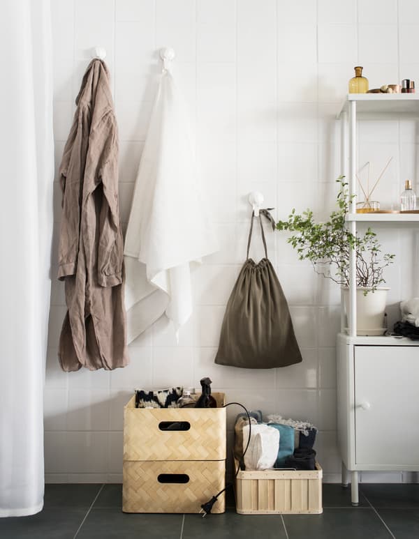 Three straw baskets are stacked on a bathroom floor, holding bulky items like a hair dryer and rolled towels.