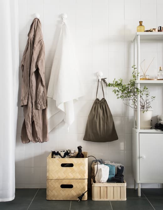 Three straw baskets are stacked on a bathroom floor, holding bulky items like a hair dryer and rolled towels.