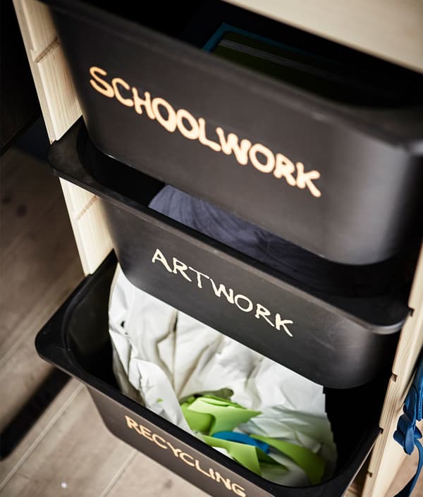 Three TROFAST black plastic boxes labeled and organised by function such as schoolwork, artwork and recycling.