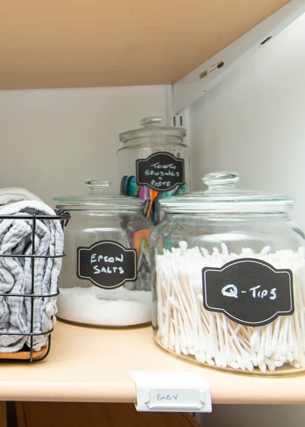 Three VARDAGEN jars with lids on a shelf, used to store Q-tips, Epsom salts, and toothbrushes.
