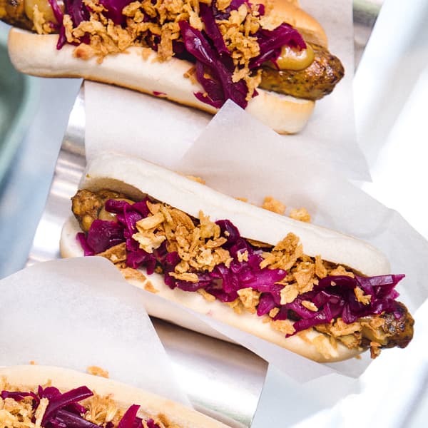 Three veggie hotdogs with pickled red cabbage, spicy mustard and fried onions waiting to be collected on a serving stand.