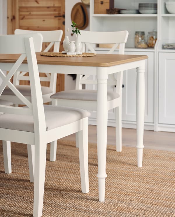 Three white chairs and a table in white/oak with tubular steel legs on a jute rug. Two white high cabinets in the background.