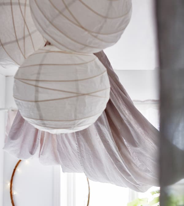 Three white paper lanterns hang from the ceiling of a bright white bedroom.