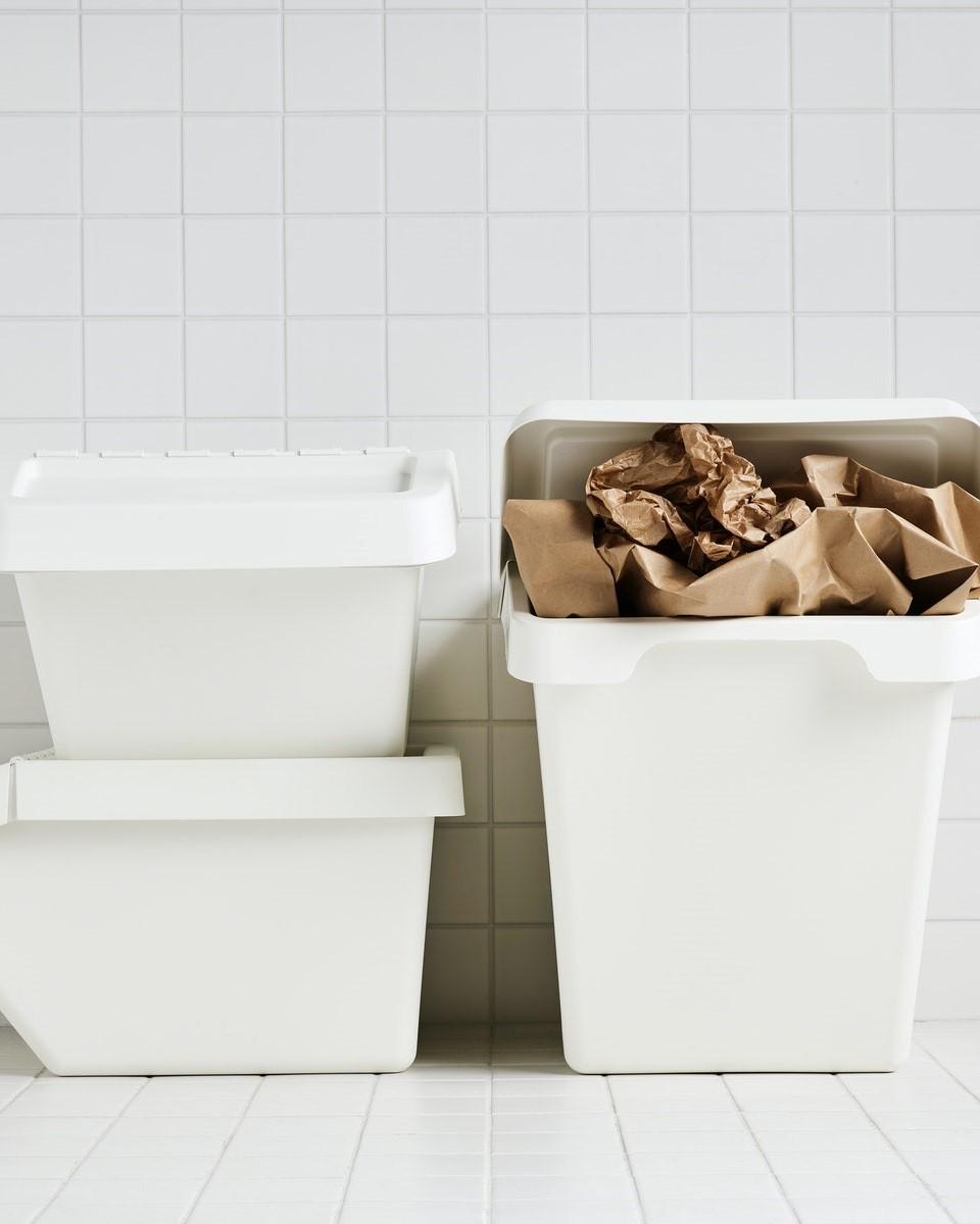 Three white SORTERA bins in a white tiled room where one is stuffed with brown paper.