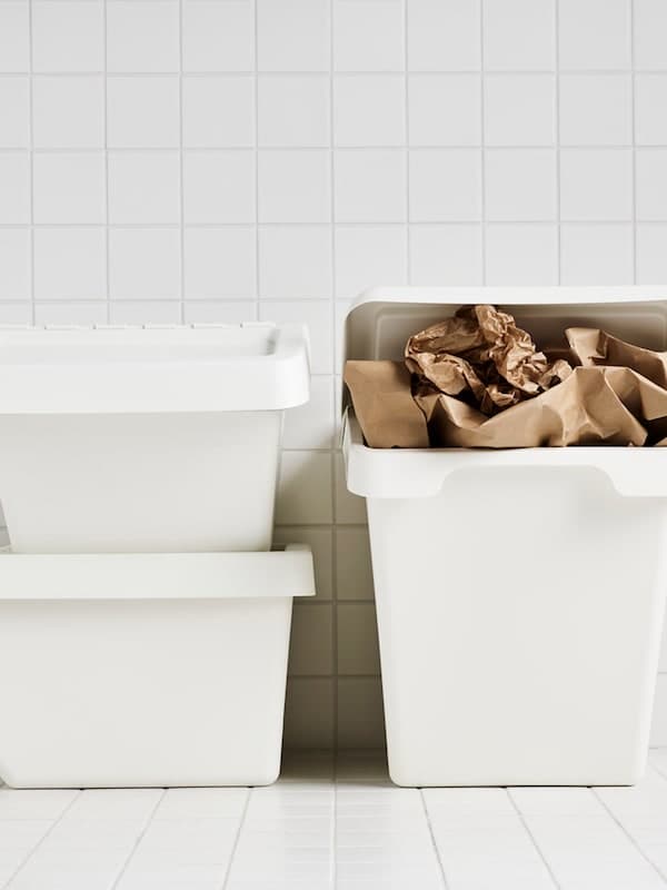 Three white SORTERA bins in a white tiled room where one is stuffed with brown paper.
