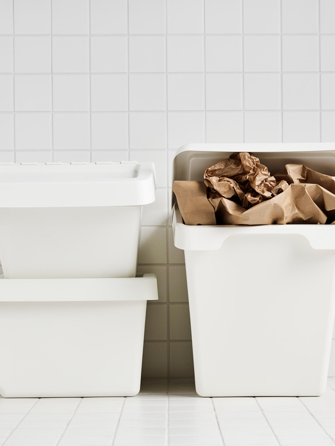 Three white SORTERA bins in a white tiled room where one is stuffed with brown paper.