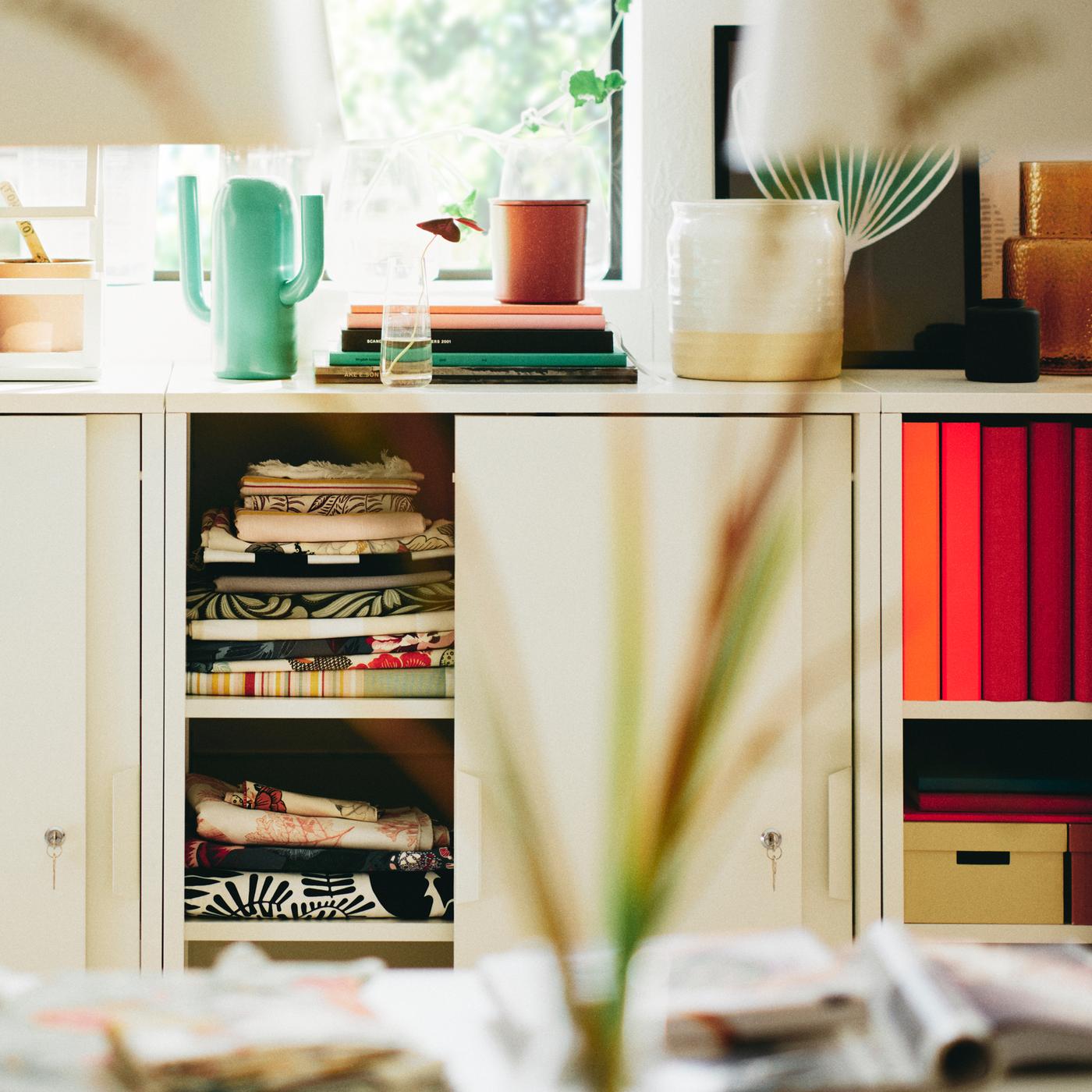Three white TROTTEN cabinets with sliding doors with a bright green ÄRTBUSKE vase/watering can on top of one of them.