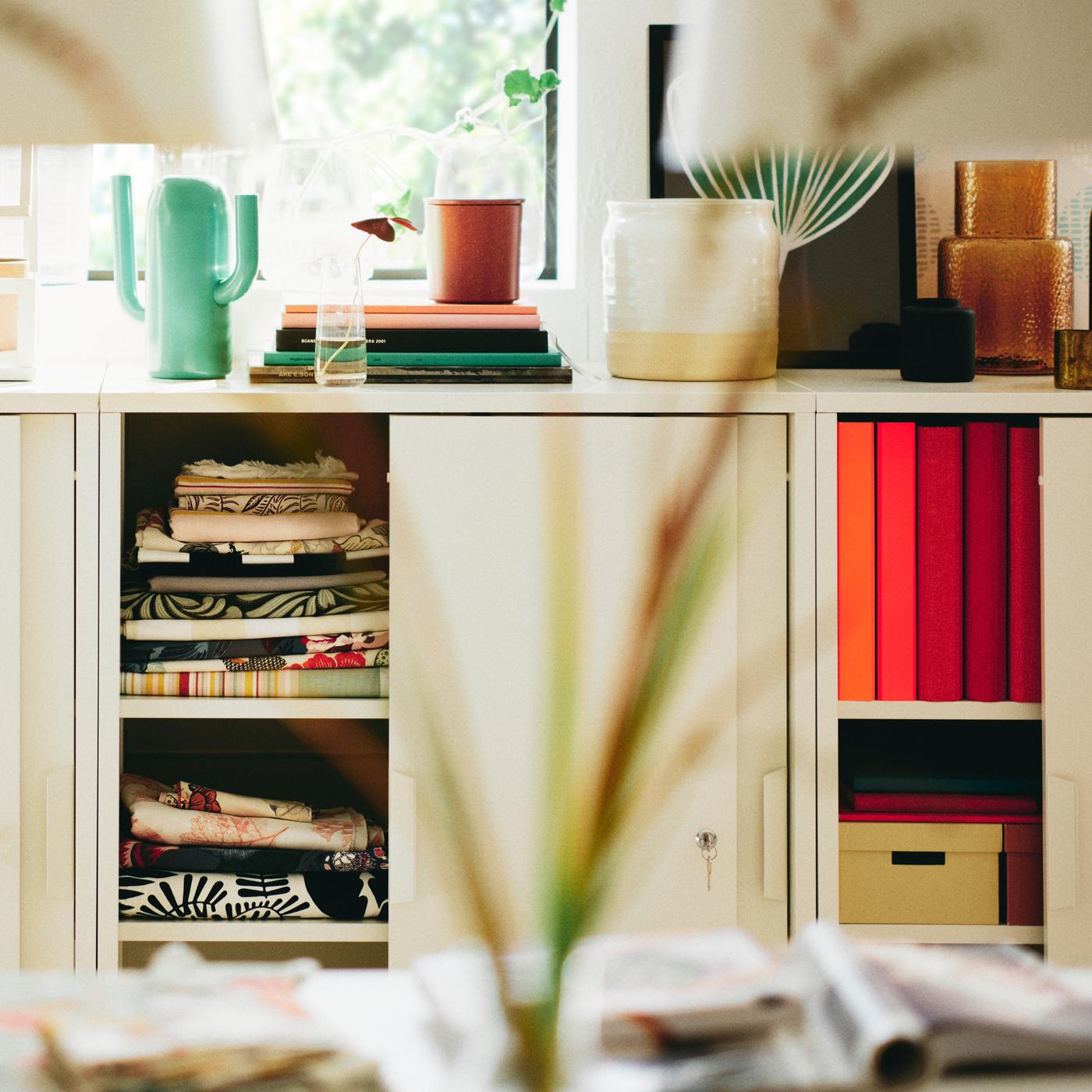 Three white TROTTEN cabinets with sliding doors with a bright green ÄRTBUSKE vase/watering can on top of one of them.