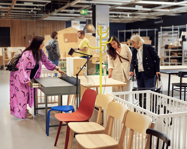 Three women in an IKEA Circular hub looking at desks next to a crib and three coloured chairs.