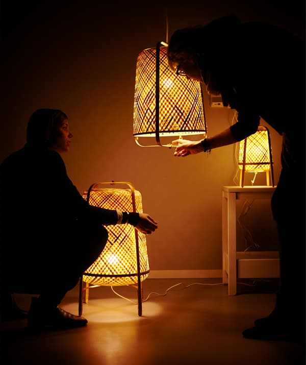 Three woven lamps lit up and two figures in the shadows.