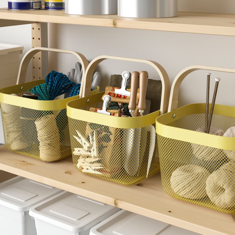 Three yellow RISATORP storage baskets with wooden handles storing various items including knitting balls of wool, gardening supplies and more, placed on an IVAR wooden shelf.