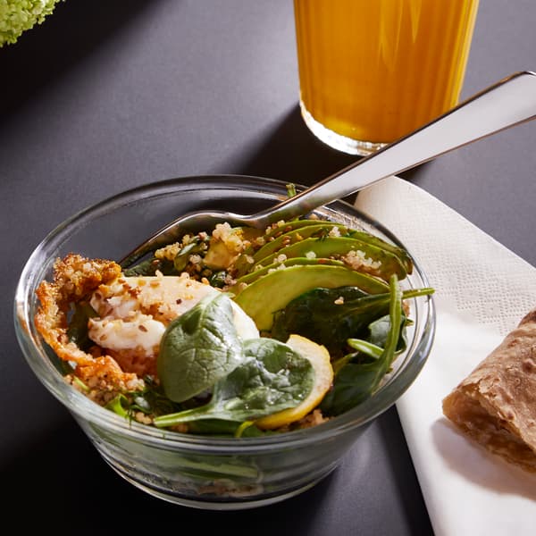 Tigela de vidro com uma salada verde e um copo de sumo de laranja em segundo plano.