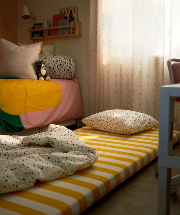 Tilam dengan bantal dan duvet dibentangkan di atas lantai di sisi katil kanak-kanak. Cahaya yang malap dan langsir bilik tidur tertutup.