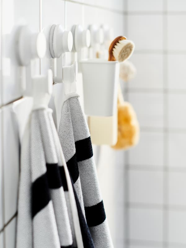 Tiled bathroom wall with a row of TISKEN suction-cup hooks, holding towels, a scrubber, and similar bathroom accessories.