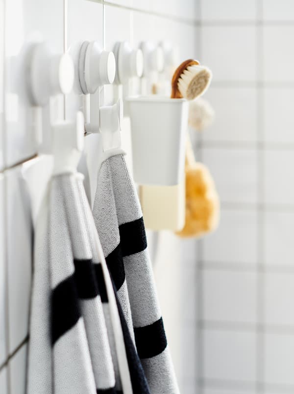 Tiled bathroom wall with a row of TISKEN suction-cup hooks, holding towels, a scrubber, and similar bathroom accessories.