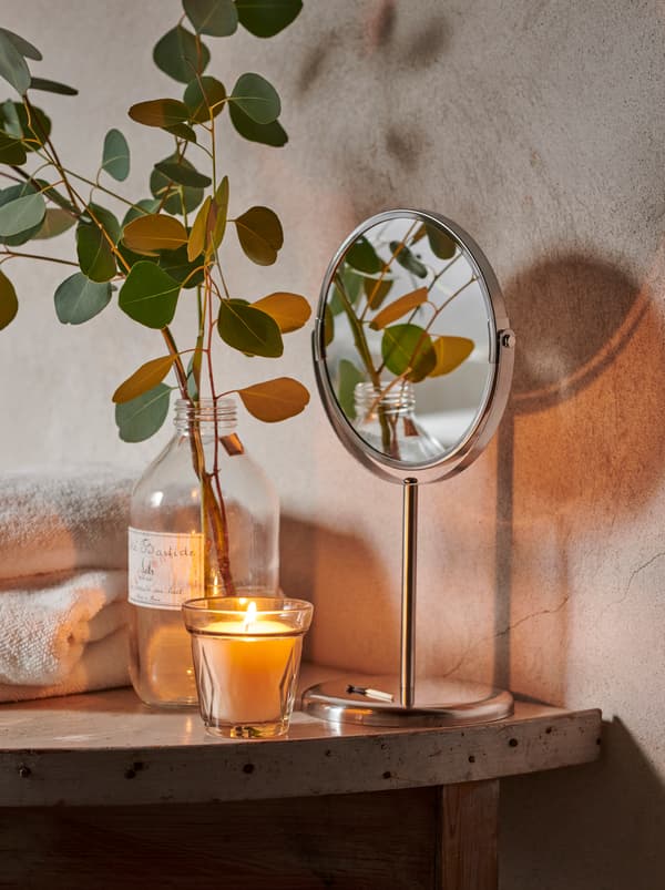 Tindanan tuala, lilin VÄLDOFT dan botol kaca yang mengandungi tangkai daun eucalyptus di atas para di dalam bilik mandi ala desa.