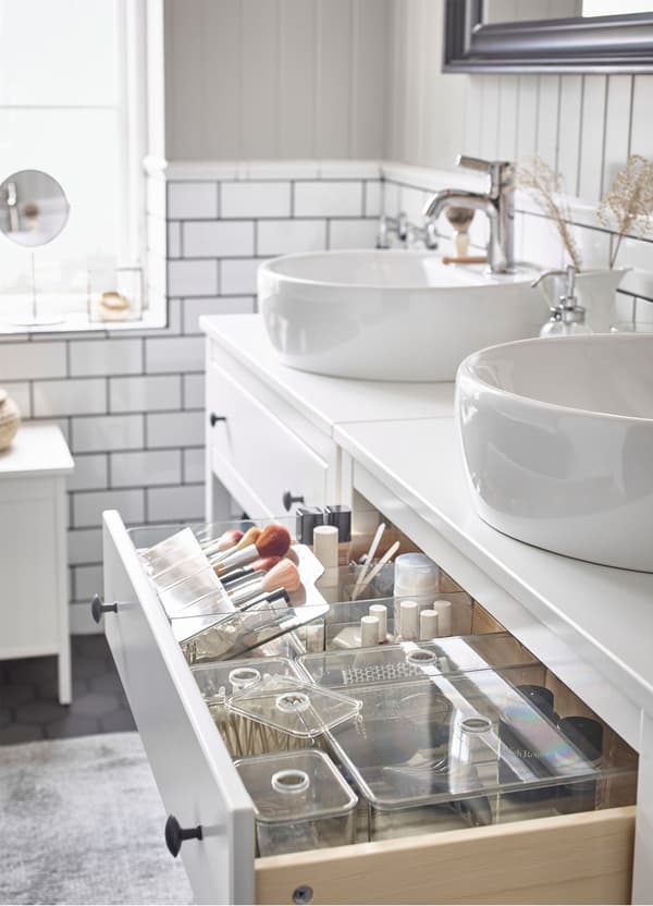 Tiroir d’un meuble lavabo ouvert, dans lequel on voit des boîtes transparentes IKEA GODMORGON avec couvercle, remplies d’accessoires de toilette.