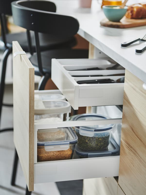 Tiroir ouvert d’un îlot de cuisine, avec sa façade ASKERSUND, laissant apparaître une solution de rangement à deux niveaux avec des couverts et des contenants pour aliments.