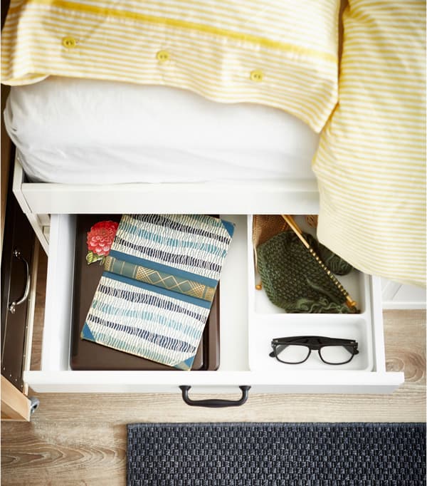 Tiroir ouvert, sur le côté du lit, avec livre et lunettes à l’intérieur.