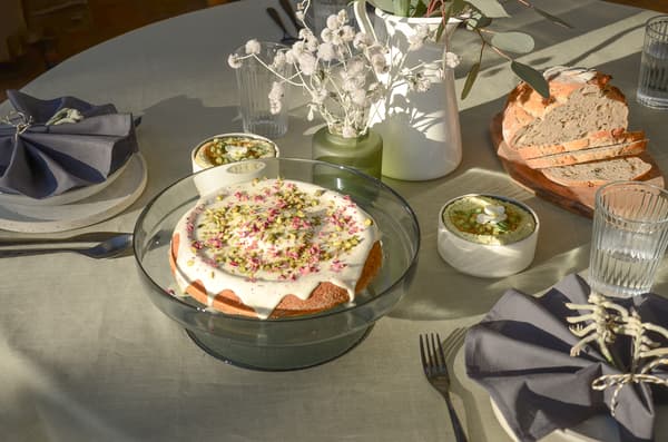 Tisch mit Kuchen, Dips, Brot, Wassergläsern, Besteck, Servietten und Vasen mit Trockenblumen und Eukalyptus.