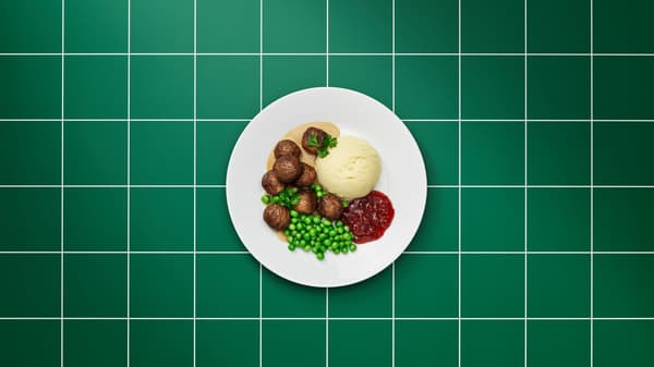 Tiszta fehér tányéron húsmentes húsgolyók, barnamártás, burgonyapüré, áfonyalekvár, zöldborsó és petrezselyemlevelek.