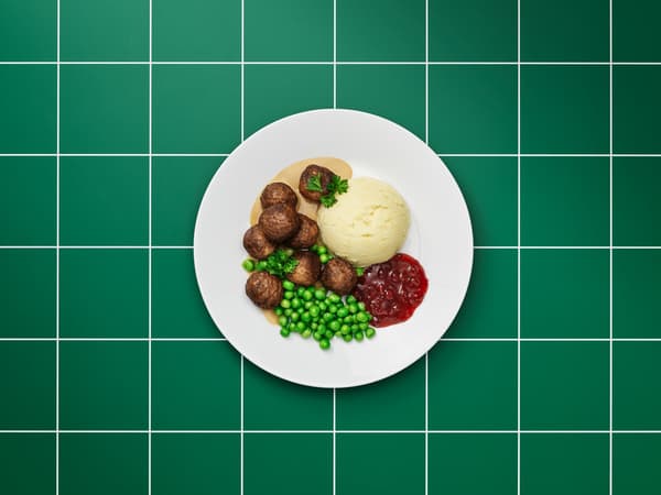 Tiszta fehér tányéron húsmentes húsgolyók, barnamártás, burgonyapüré, áfonyalekvár, zöldborsó és petrezselyemlevelek.