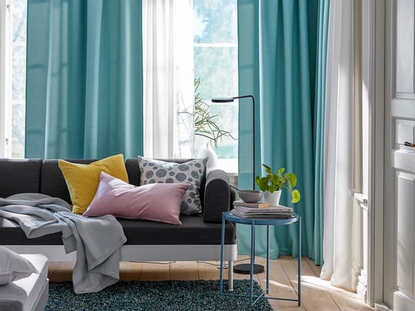 ターコイズのカーテンとグレーソファを組み合わせたモダンリビング。ピンクのクッションで彩りをプラス。